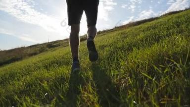 年轻人在蓝色天空背景下运行过绿色的小山。日落时分，男运动员慢跑性质。体育跑步慢跑上山室外日出与耀斑。越野训练。慢动作